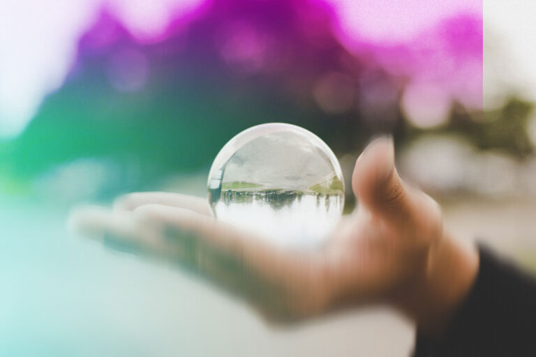 A hand holding a glass ball with reflection of street in it.