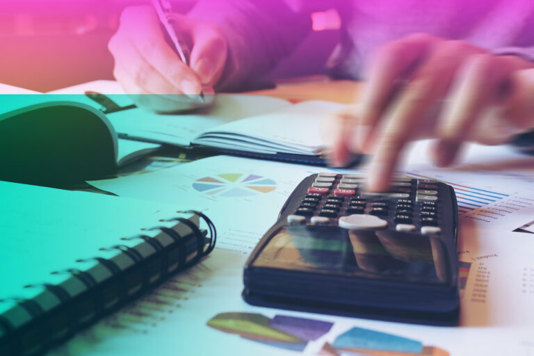 A person working a desk with a notebook, papers and a calculator.