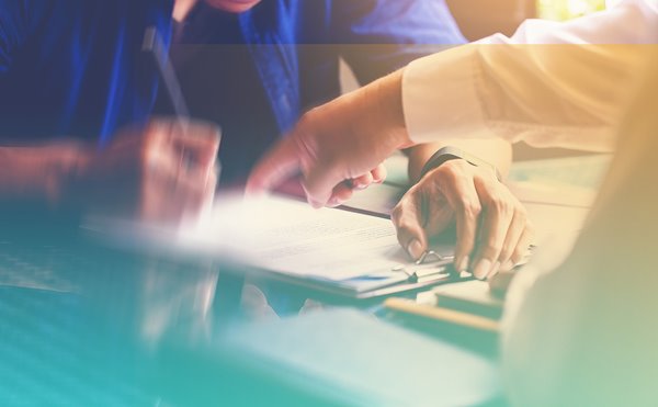 A person pointing at a document on a clipboard held by another person who is signing it.