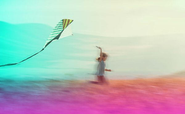 A child running through a field flying a kite.