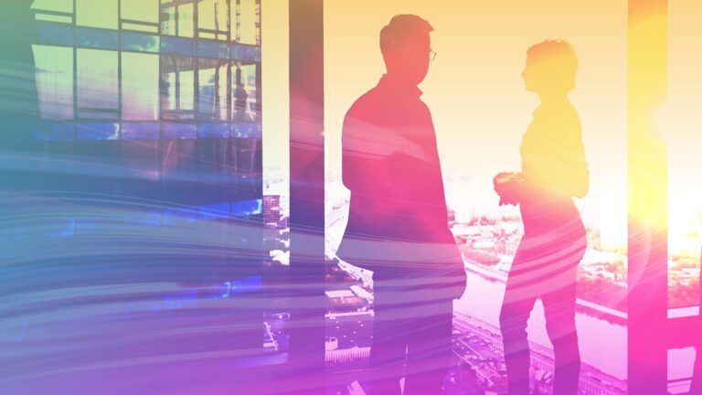 Two people in an office by the window talking.